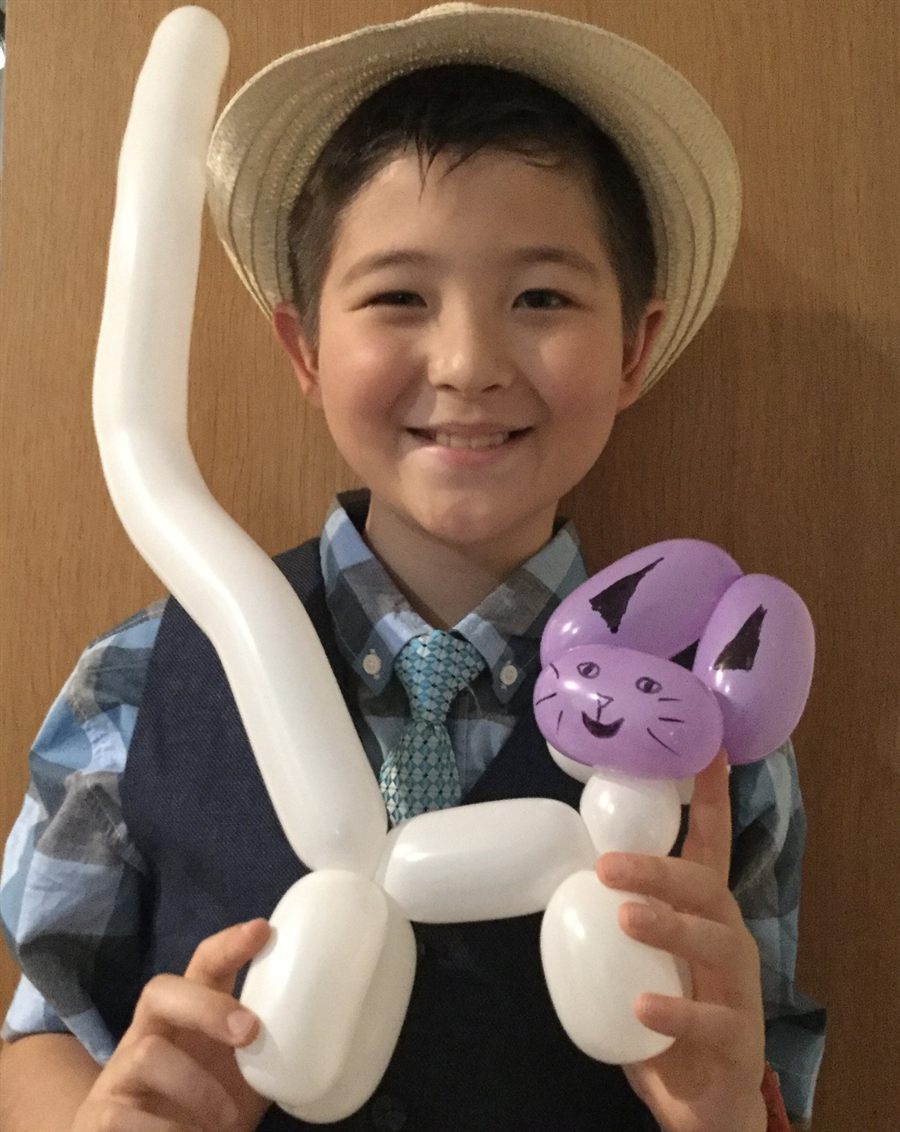 Young Elijah in a straw hat holding a white balloon cat with a lilac head, drawn-on whiskers and a very long tail