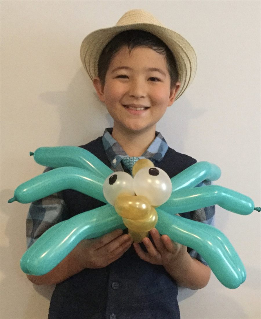 Young Elijah in a straw hat holding a teal balloon spider with eight legs and big white eyes